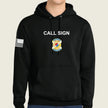 A black pullover hoodie worn by a model, featuring the words 'CALL SIGN' in white across the chest, a gold and blue army badge graphic below it, and a black-and-white American flag on the right sleeve.