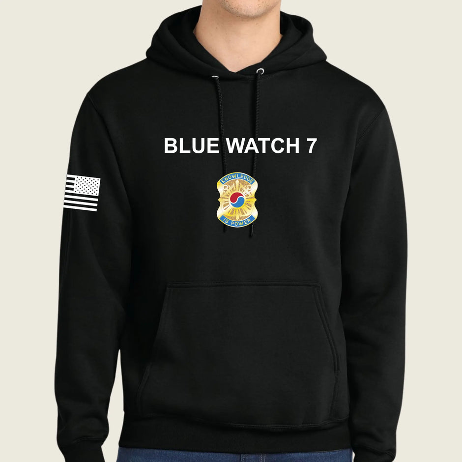 A black pullover hoodie worn by a model, featuring 'BLUE WATCH 7' in white text on the chest, a army graphic below it, and a black-and-white American flag patch on the right sleeve.