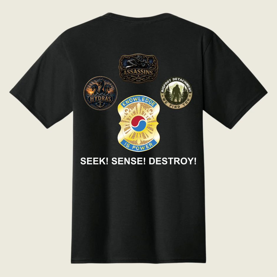 A black short-sleeve t-shirt shown from the back, featuring four military-style insignia patches and the text 'SEEK! SENSE! DESTROY!' printed in white on a light beige background.