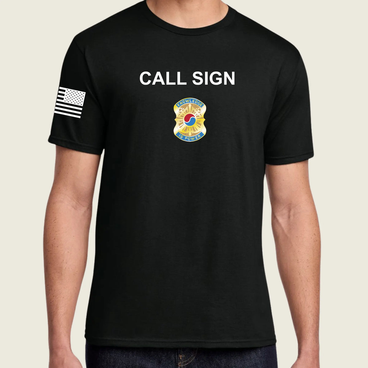 A man wearing a black short-sleeve t-shirt with 'CALL SIGN' printed in white across the chest, a colorful graphic below it, and a black-and-white American flag patch on the right sleeve, shown against a light beige background.