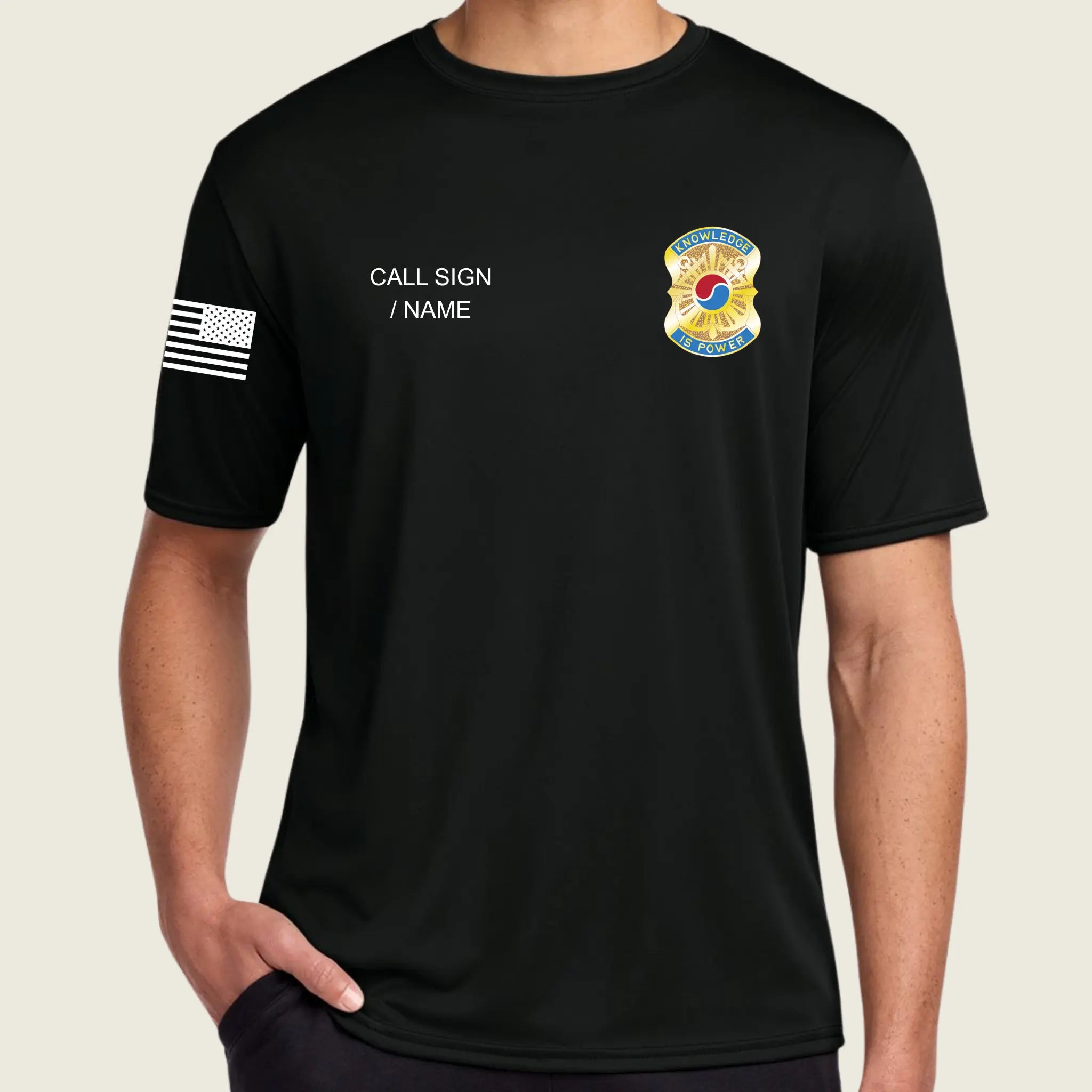 A man wearing a black short-sleeve t-shirt with customizable white text on the left chest, a black and white American flag graphic on the right sleeve, and a yellow and blue badge on the left chest.