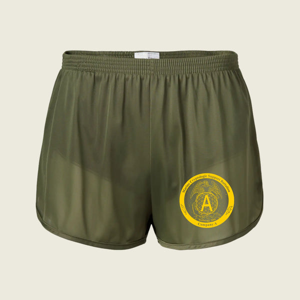 Olive green athletic shorts with a yellow circular emblem printed on the lower left leg, shown against a light beige background.