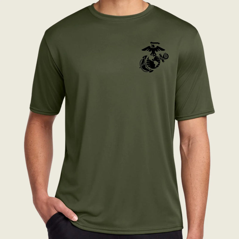 A man wearing an olive green short-sleeve athletic t-shirt with a black US Marine Corps Eagle, Globe, and Anchor emblem printed on the left chest, set against a solid light beige background.